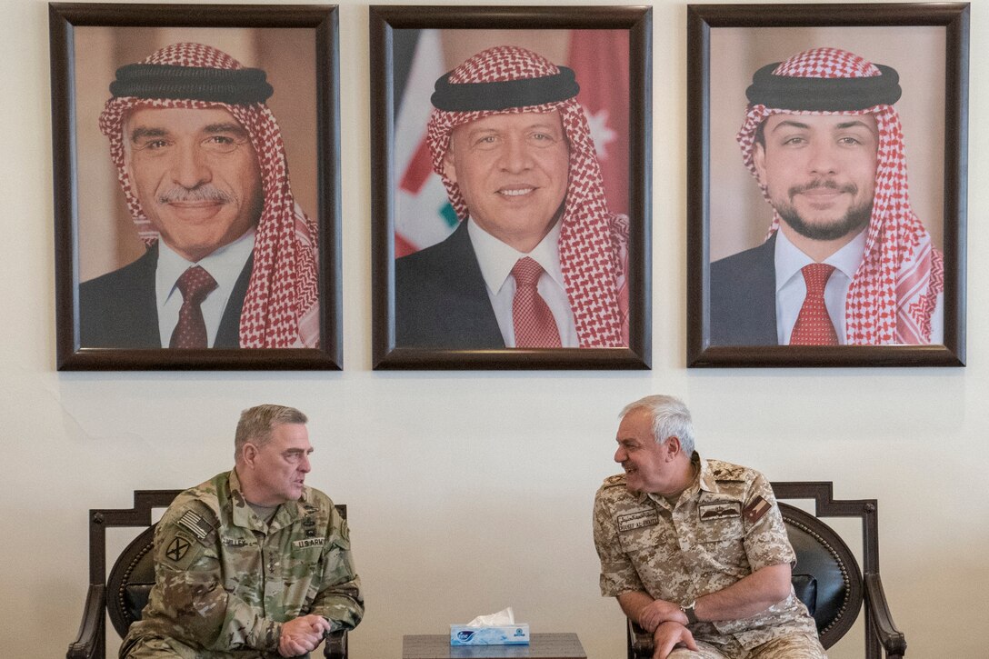 Two military leaders sit in chairs and talk to each other.