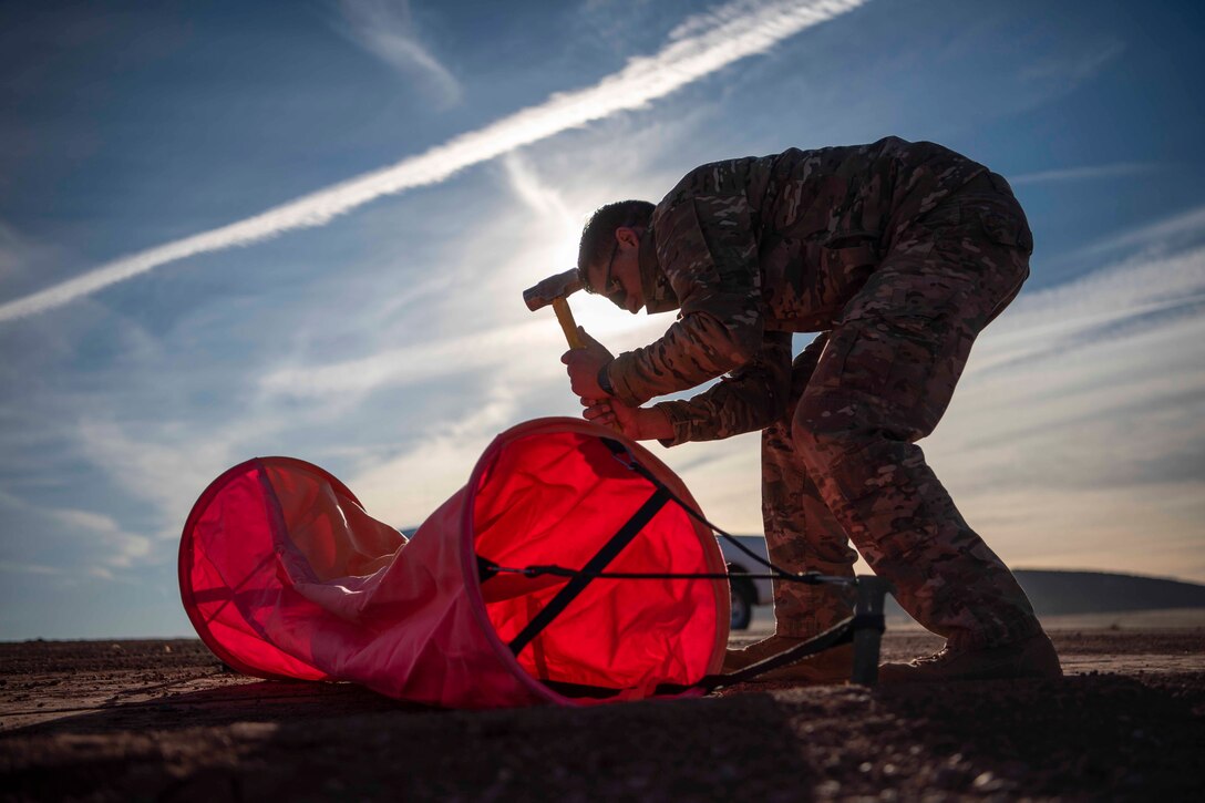 An airman hammers down a red tube to the ground.