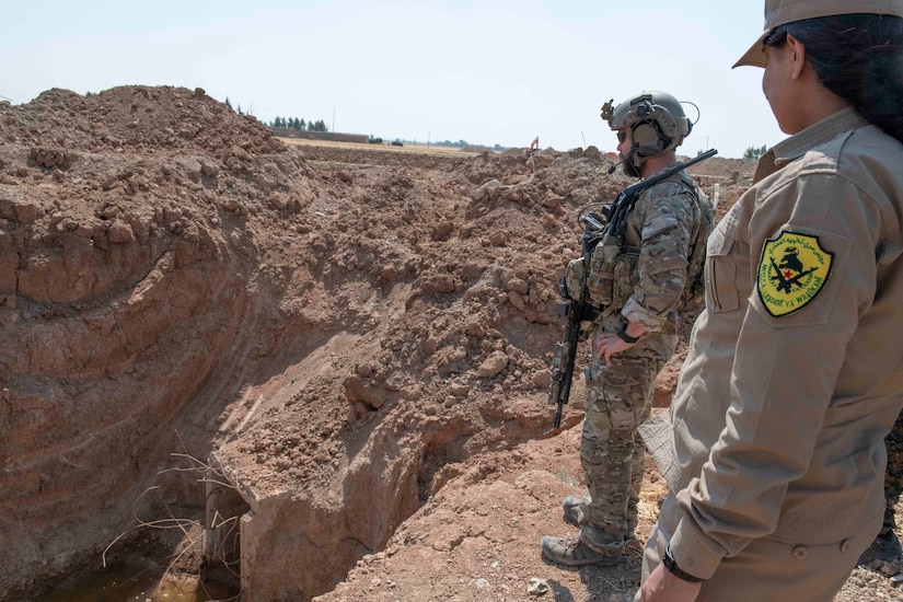 Two service members look down onto a construction site.