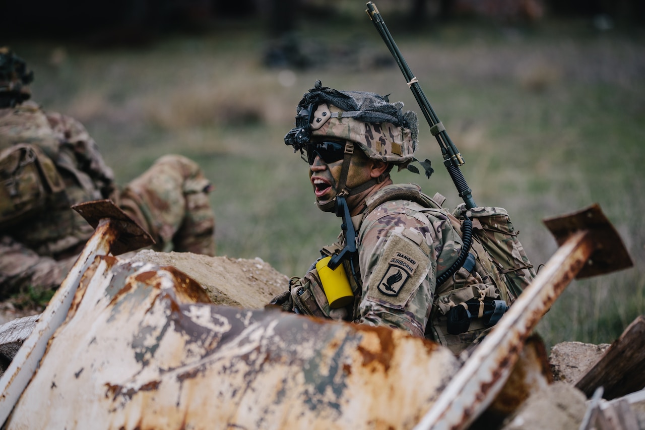 A soldier shouts while crouched behind an obstacle during training.