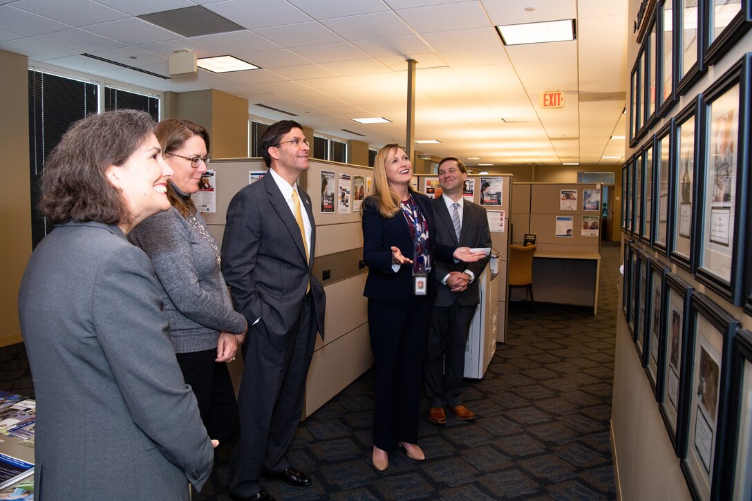 A group of people stand together and look at framed pictures on a wall.