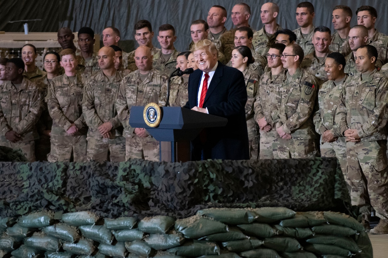 A man speaks from behind a podium surrounded by military members.