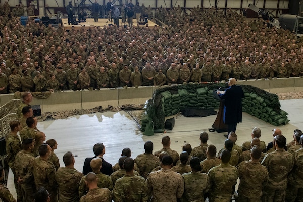 A man speaks from behind a podium surrounded by military members.