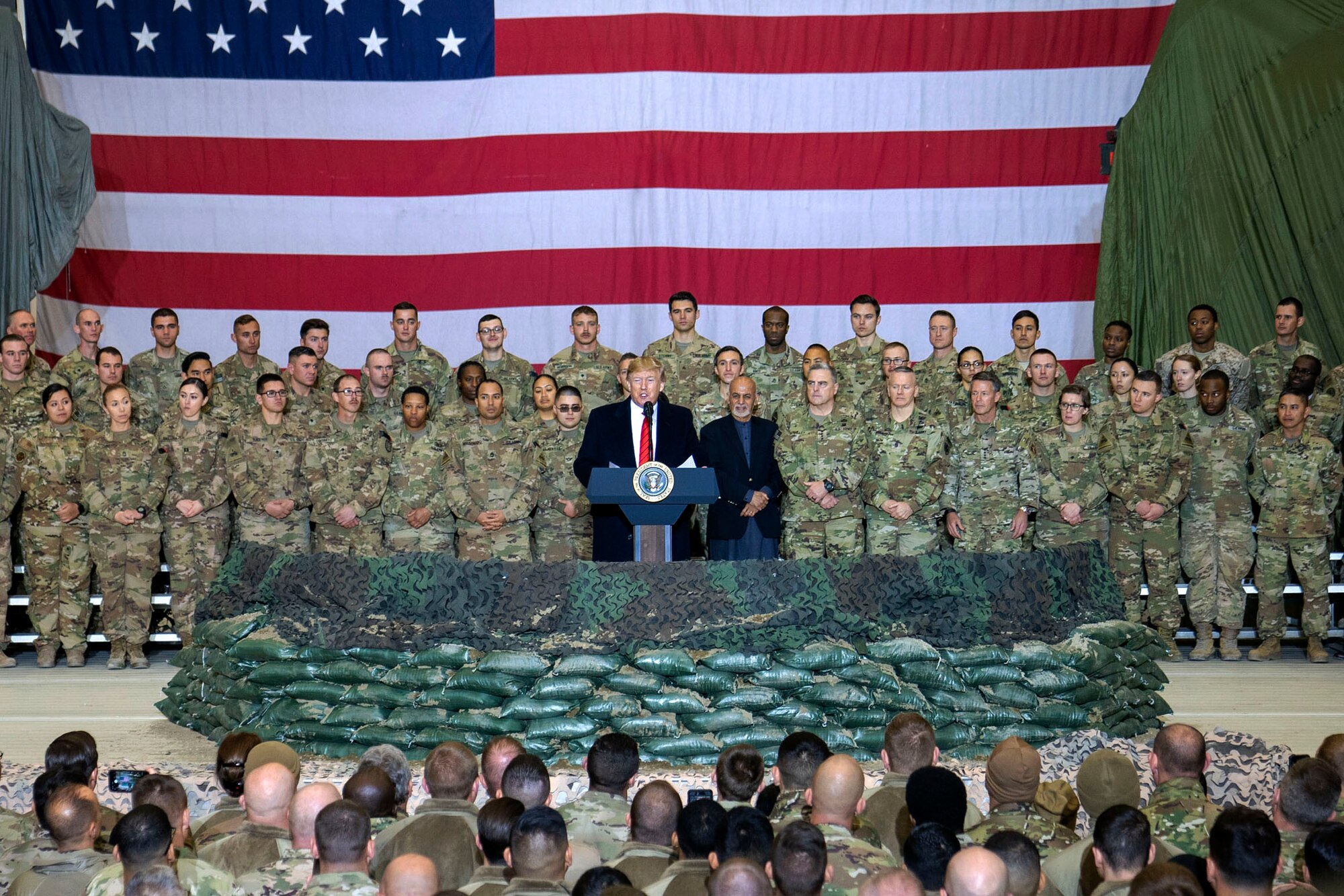 A man speaks from behind a podium  surrounded by military members.