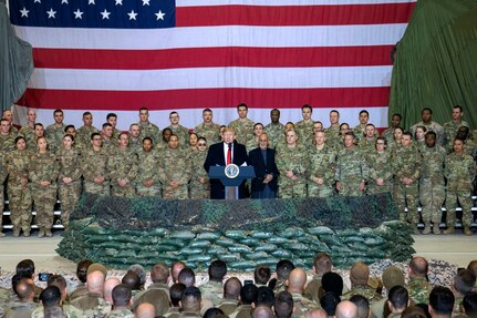 A man speaks from behind a podium  surrounded by military members.