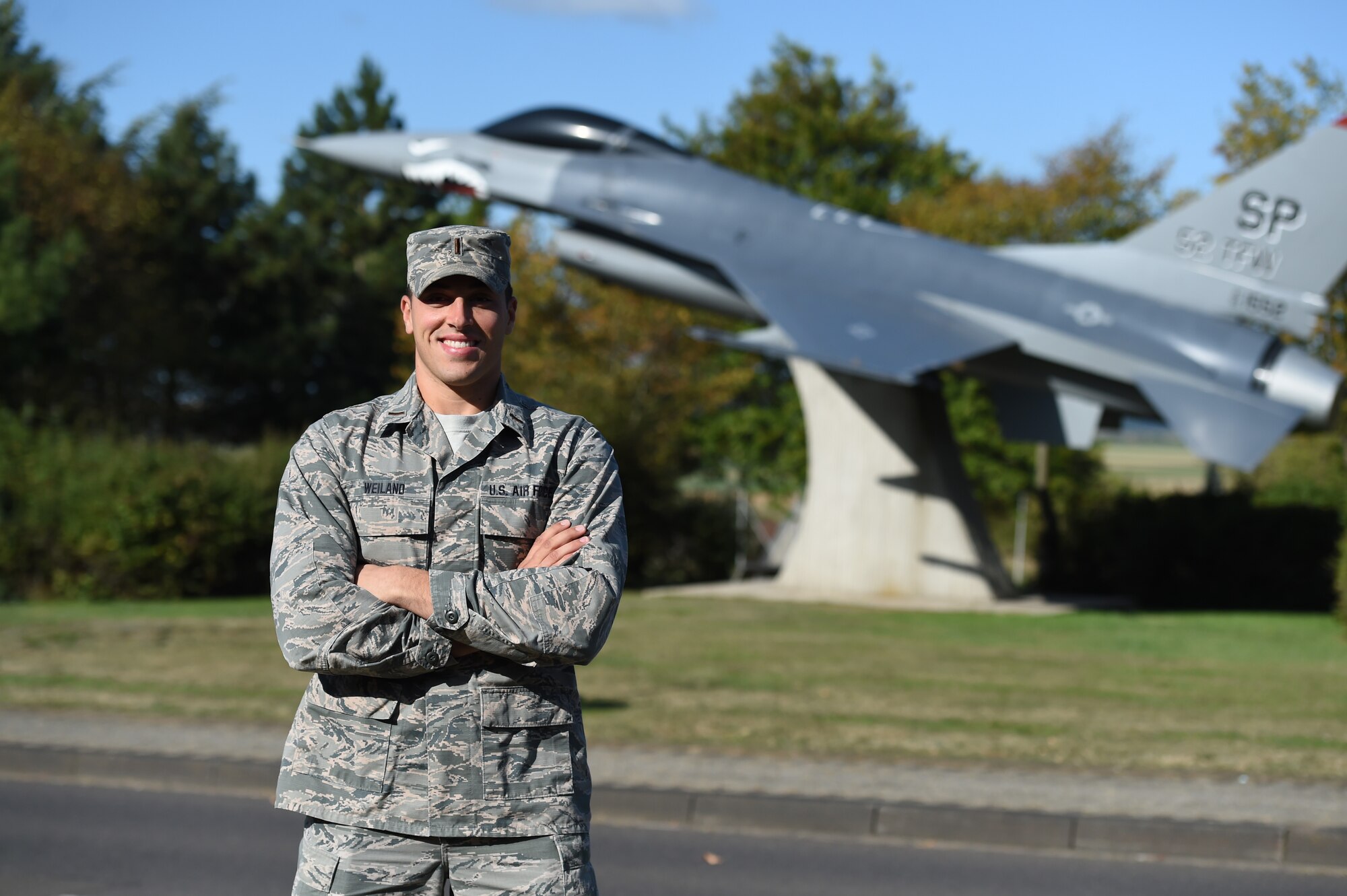2nd Lt. Nick Weiland poses in front of an F-16 static display at his former unit September 19, 2019, at Spangdahlem Air Base, Germany. Weiland spent two years stationed in Germany as an enlisted Airman and returned in 2019 as an officer with the 132d Logistics Readiness Squadron. (U.S. Air National Guard photo by Staff Sgt. Michael J. Kelly)