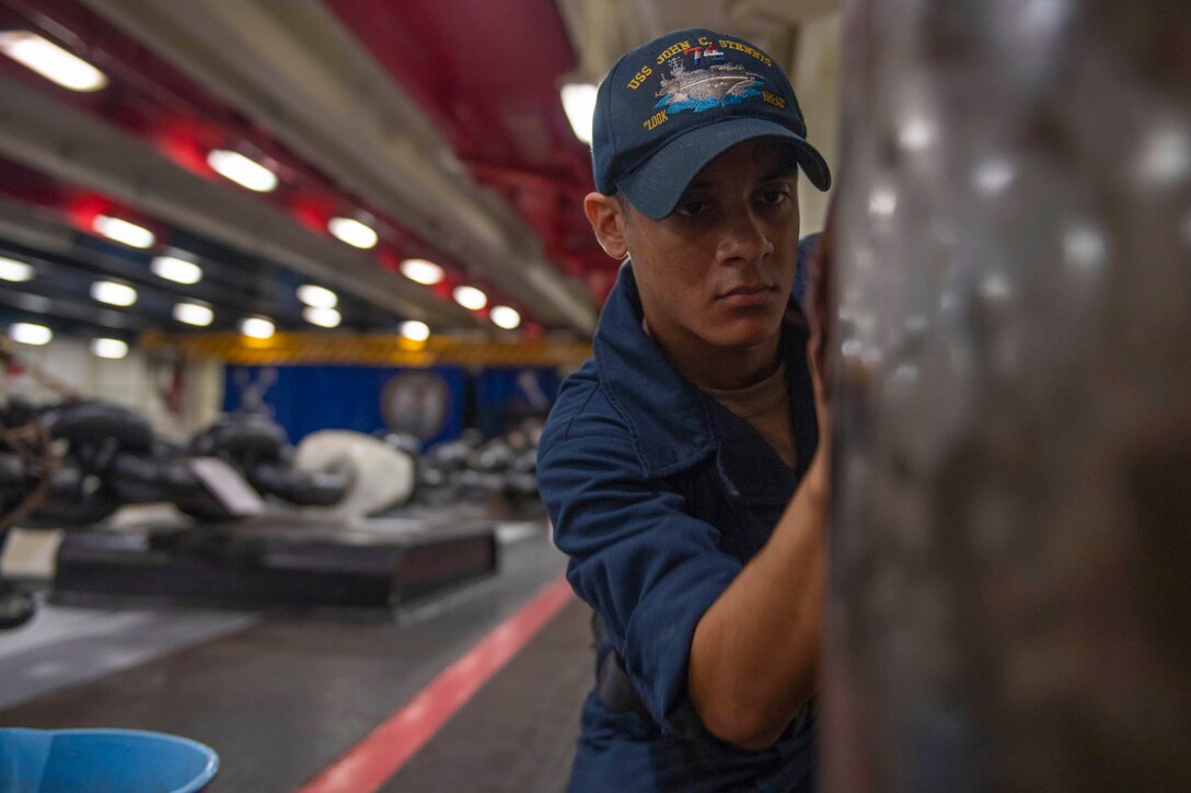 A sailor sands a capstan.