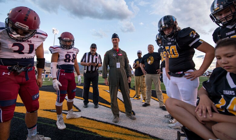 Alamogordo and Demming High School football players and Lt. Col. Ryan Typolt, 29th Attack Squadron commander, look at the pre-game coin toss results during AHS Military Appreciation Night football game, Sept. 27th, 2019, in Alamogordo, N.M. Typolt was invited to swear-in nine individuals into the Delayed Entry Program. (U.S. Air Force photo by Staff Sgt. Christine Groening)