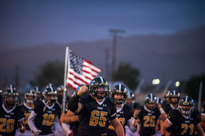 The Alamogordo High School Football Team run with the American flag prior to an AHS Military Appreciation Night football game,  Sept. 27th, 2019, in Alamogordo N.M. Holloman Air Force Base leadership was invited to the event to interact with the local community and enlist nine individuals into the Delayed Entry Program. (U.S. Air Force photo by Staff Sgt. Christine Groening)