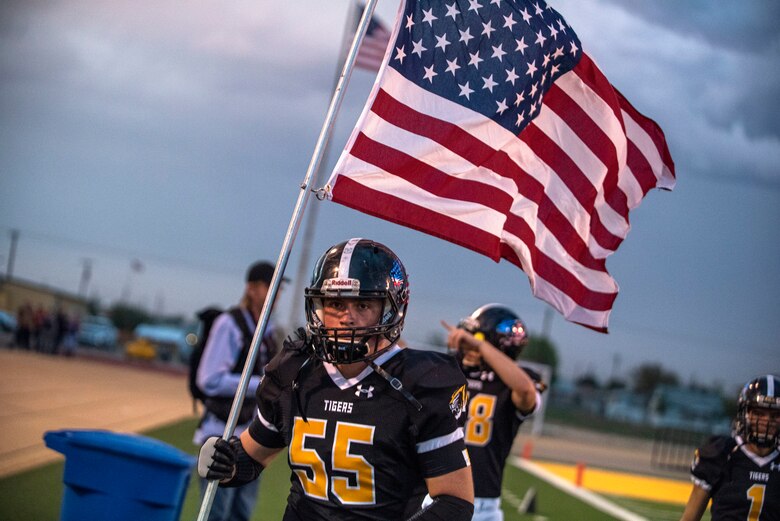 An Alamogordo High School Football player carries the American flag prior to an AHS Military Appreciation Night football game, Sept. 27th, 2019, in Alamogordo N.M. Holloman Air Force Base leadership was invited to the event to interact with the local community and enlist nine individuals into the Delayed Entry Program. (U.S. Air Force photo by Staff Sgt. Christine Groening)