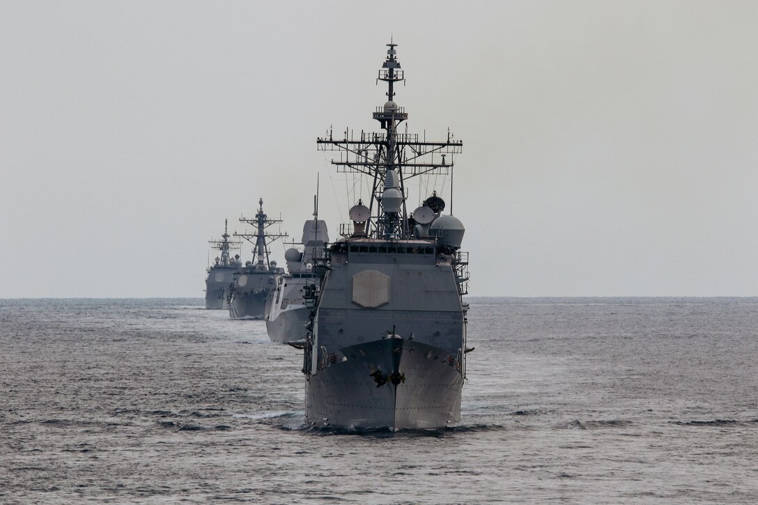 Four military ships line up behind each other in the ocean.