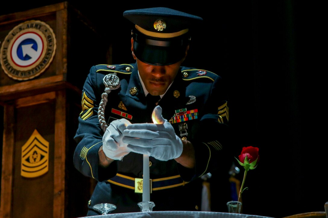 A soldier lights a candle at a table set with a rose.