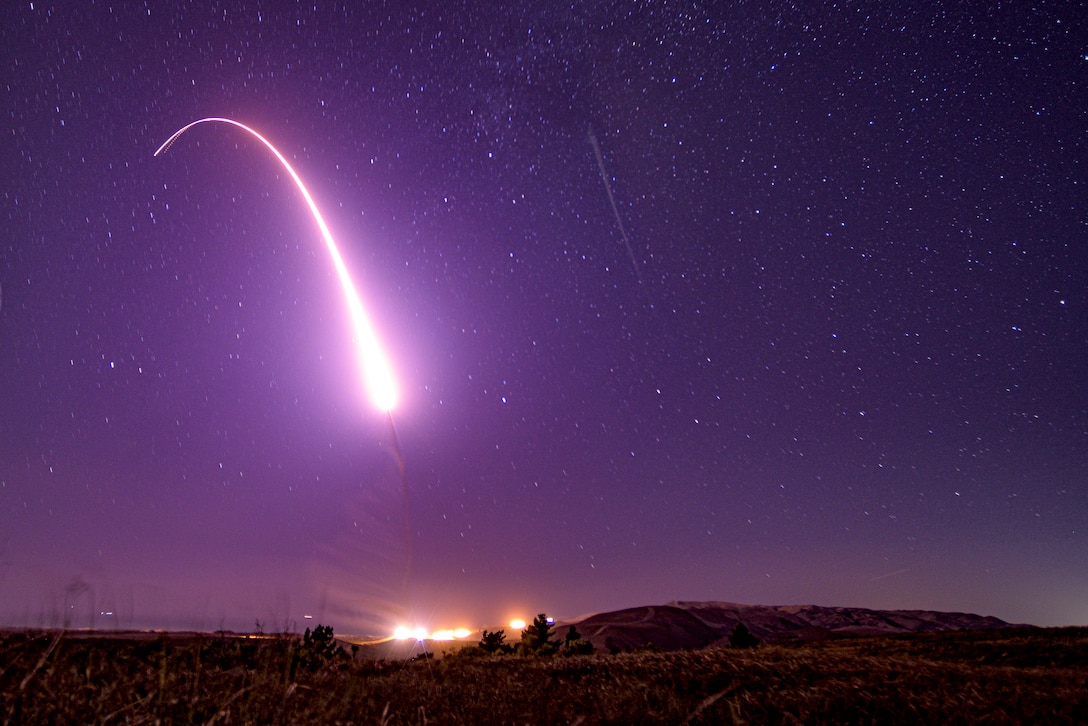 A missile launch creates a curve of light in a purple night sky.