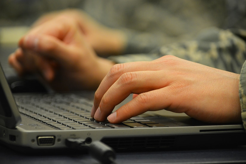 A service member\s hands on top of a laptop computer keyboard.