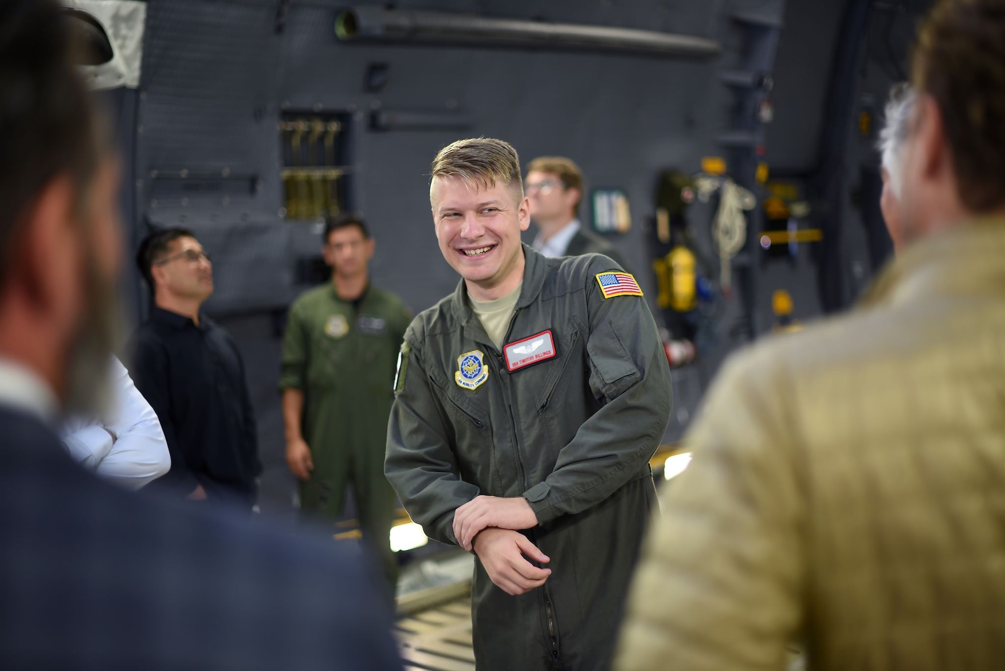 A blonde military man in a flightsuit speaks with men in suits inside of the cargo bay of a C-5M Super Galaxy. He is smiling