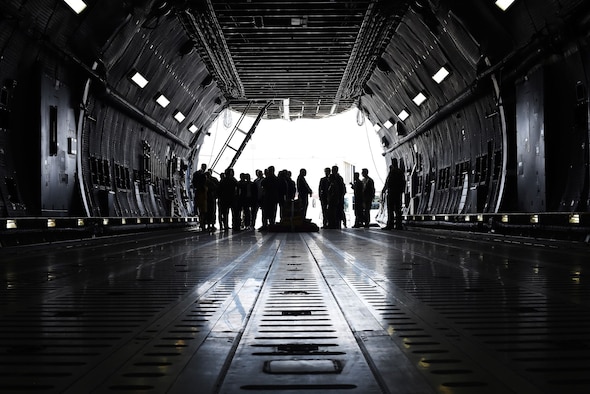 A gaggle of civilians and military members are silhouetted against the bright sunlight outside of the C-5M Super Galaxy in which they currently stand