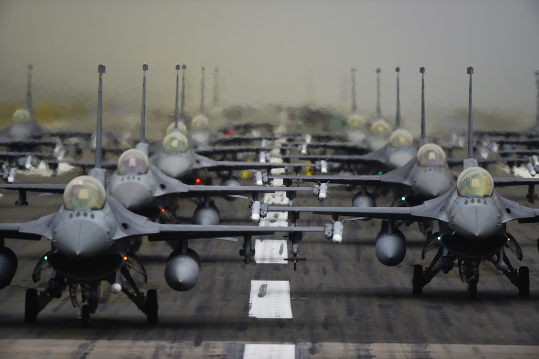 Fighter jets lines up on a runway.