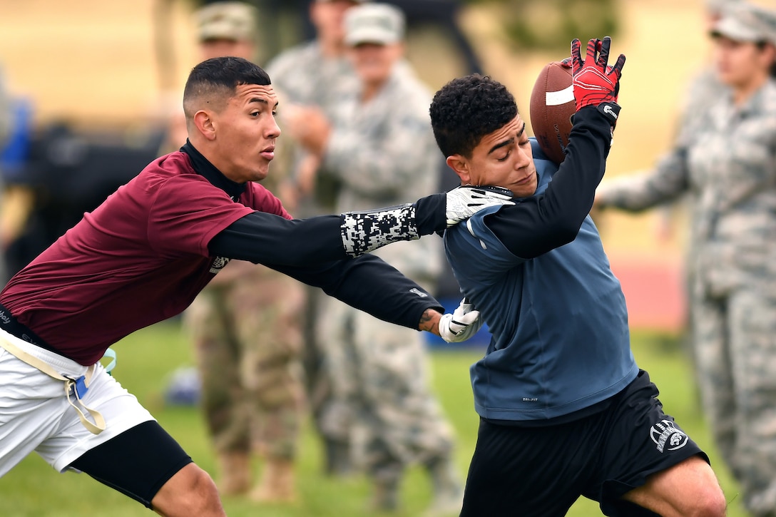 One airman grabs at another airman carrying the ball during a football game.