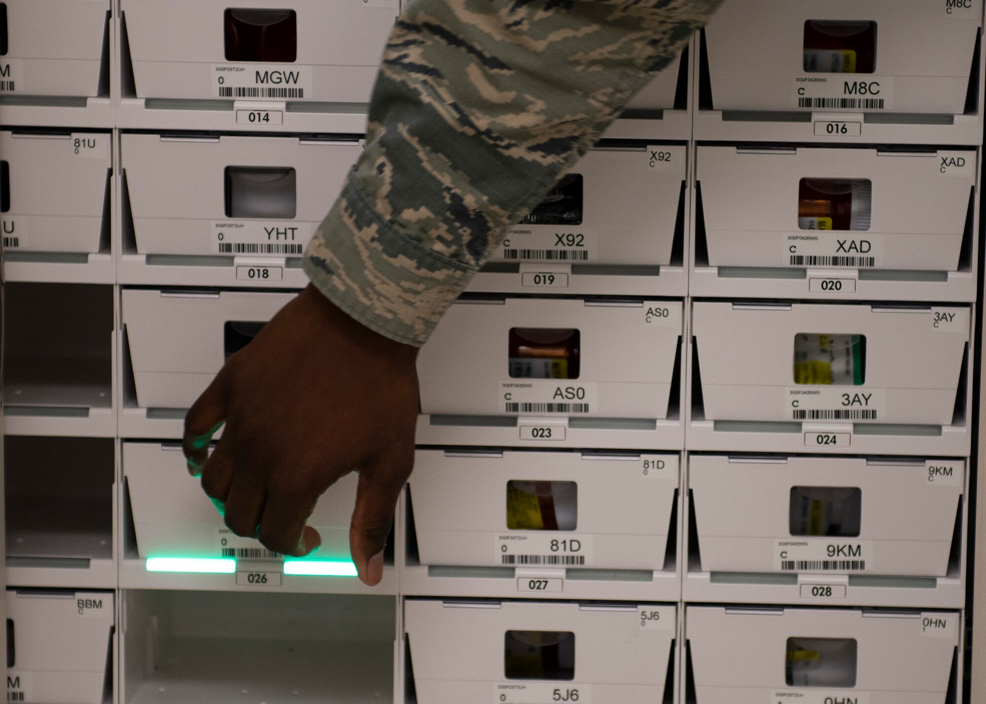 A pharmacy technician reaches for a small container that hold a patients prescription.