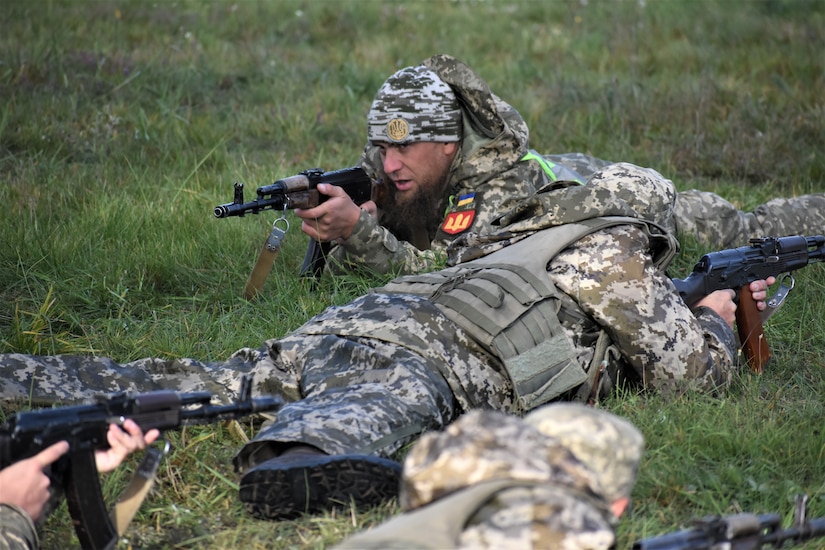 Soldiers lie on the ground and aim their rifles.