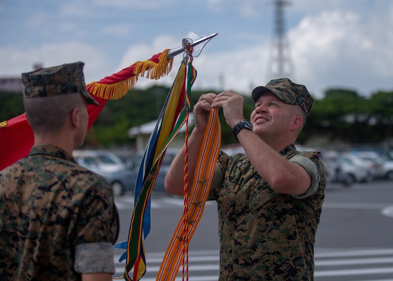 U.S. Marine Col. Michael J. Roach, Commanding Officer of 12th Marine Regiment, 3rd Marine Division, attaches a streamer to colors during the 12th Marine Regiment 92nd Anniversary Battle Colors Rededication Ceremony on Camp Hansen, Okinawa, Japan, Oct. 4, 2019. The ceremony is an opportunity for Marines to remember warriors past and to recognize contributions of service members and families to current operations. (U.S. Marine Corps photo by Lance Cpl. D’Angelo Yanez)