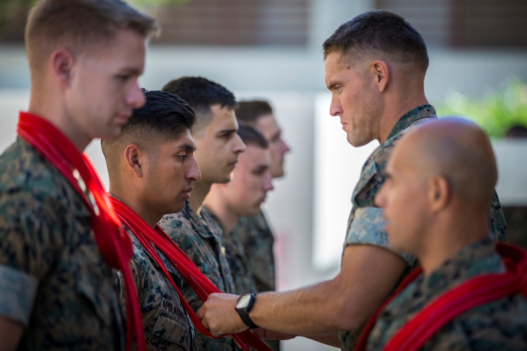 A Marine places a red scarf around the neck of another Marine.