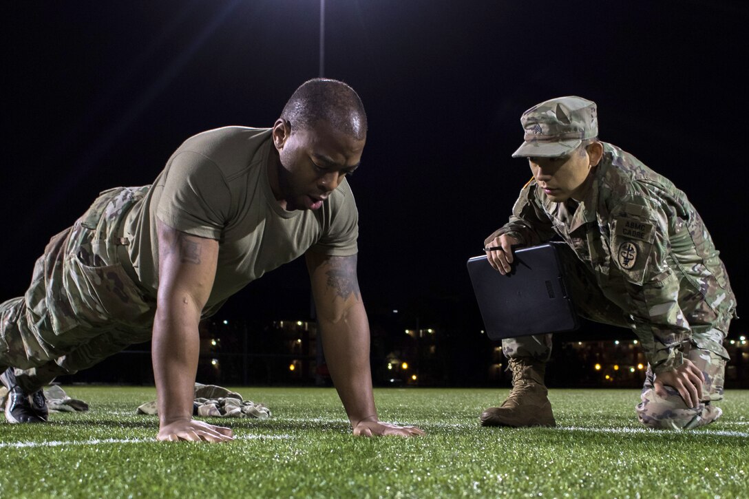 A soldier does pushups as another soldier kneels and watches.