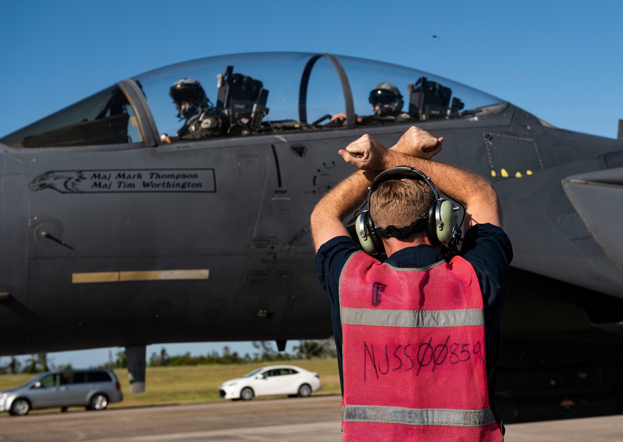 An Airman crosses his arms above his head to signal to two pilots in an aircraft in front of him.