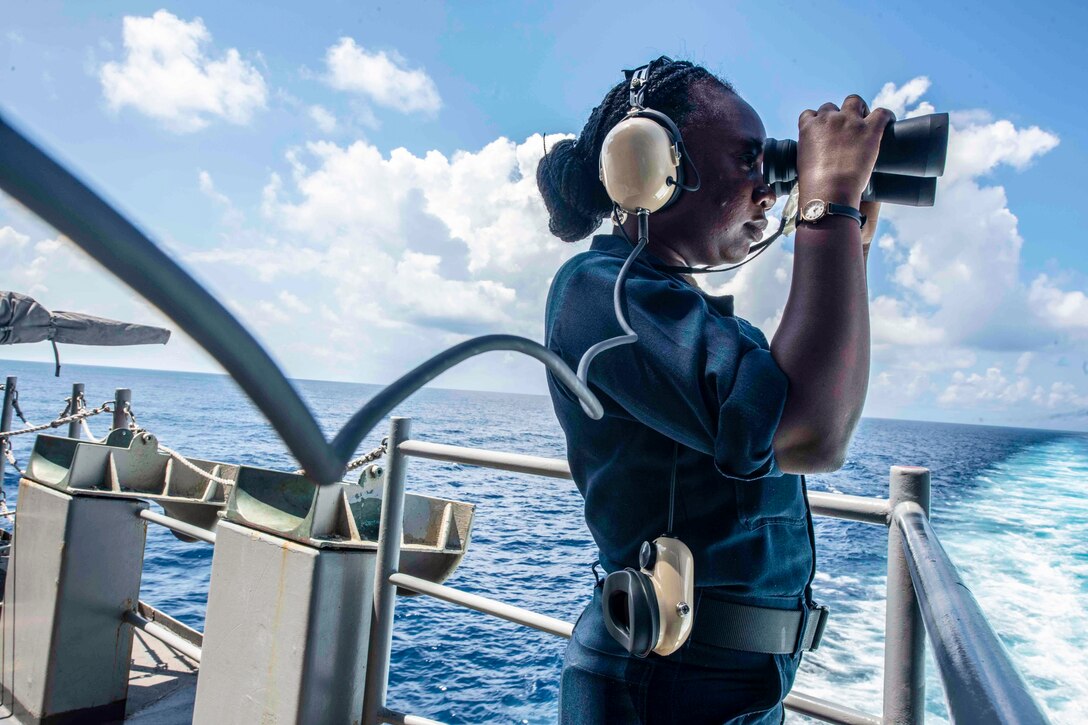 A sailor uses binoculars on a ship's deck.