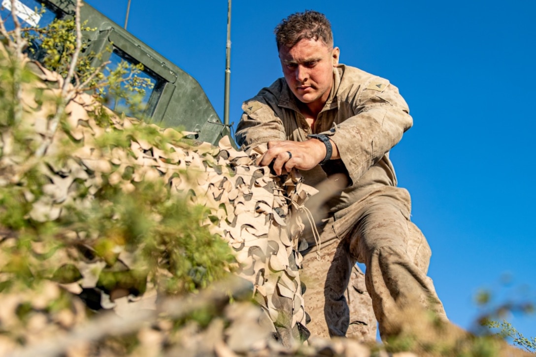 U.S. Marine Corps Lance Cpl. Trevor Kunz, a team leader with 3rd Light Armored Reconnaissance Battalion, 1st Marine Division, attaches camouflage netting to a Light Armored Vehicle during a Marine Corps Combat Readiness Evaluation (MCCRE) at Marine Corps Air Ground Combat Center Twentynine Palms, California, Sept. 6, 2019. The MCCRE is used to formally evaluate Marines on their combat readiness prior to their upcoming deployment. (U.S. Marine Corps photo by Lance Cpl. Roxanna Ortiz)