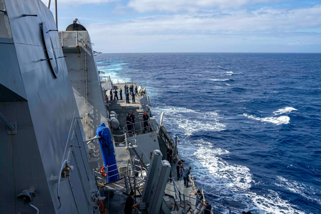 Sailors stand on the deck of a ship in the middle of the ocean.