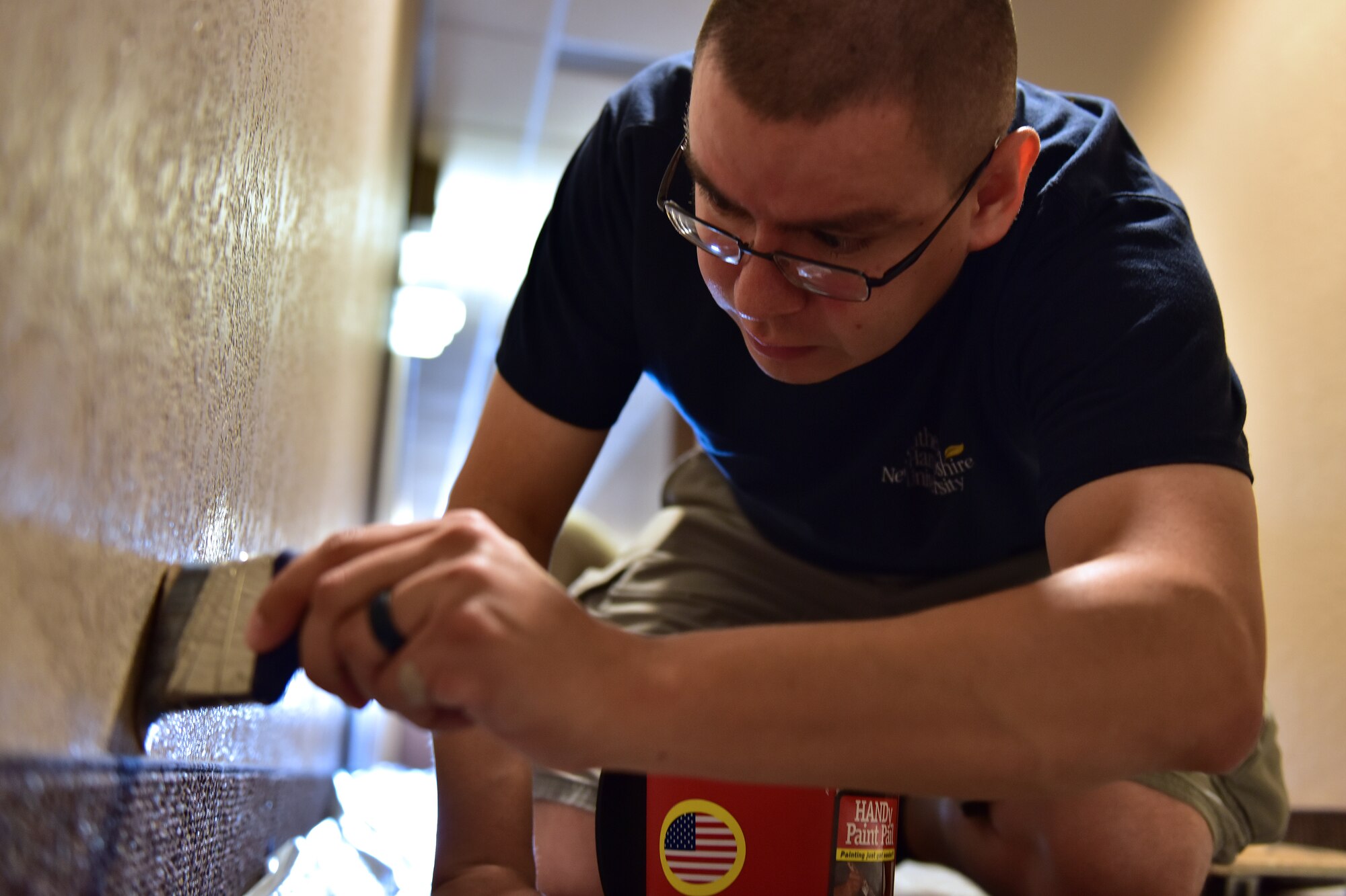 a guy paints above base boards in a hallway