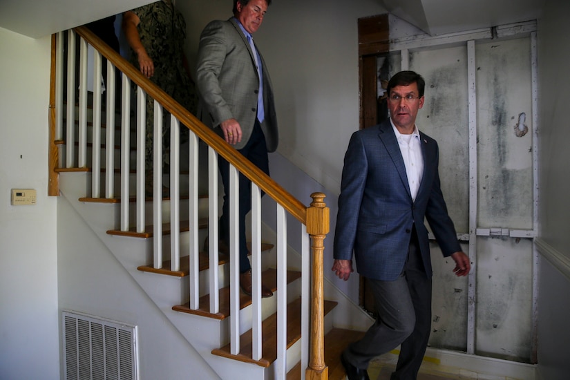 Men in suits descend a staircase in a damaged home.