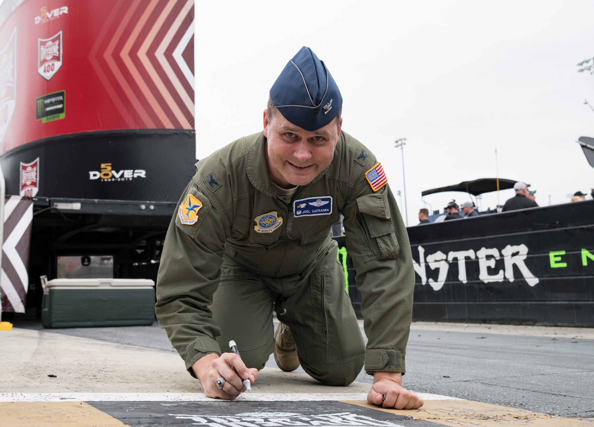 Col. Joel Safranek, 436th Airlift Wing commander, writes on the racetrack start/finish line Oct. 6, 2019, at Dover International Speedway, Dover, Del. Safranek took the opportunity to write a message on the checkered line prior to the start of the "Drydene 400" Monster Energy NASCAR Cup Series playoff race. (U.S. Air Force photo by Roland Balik)
