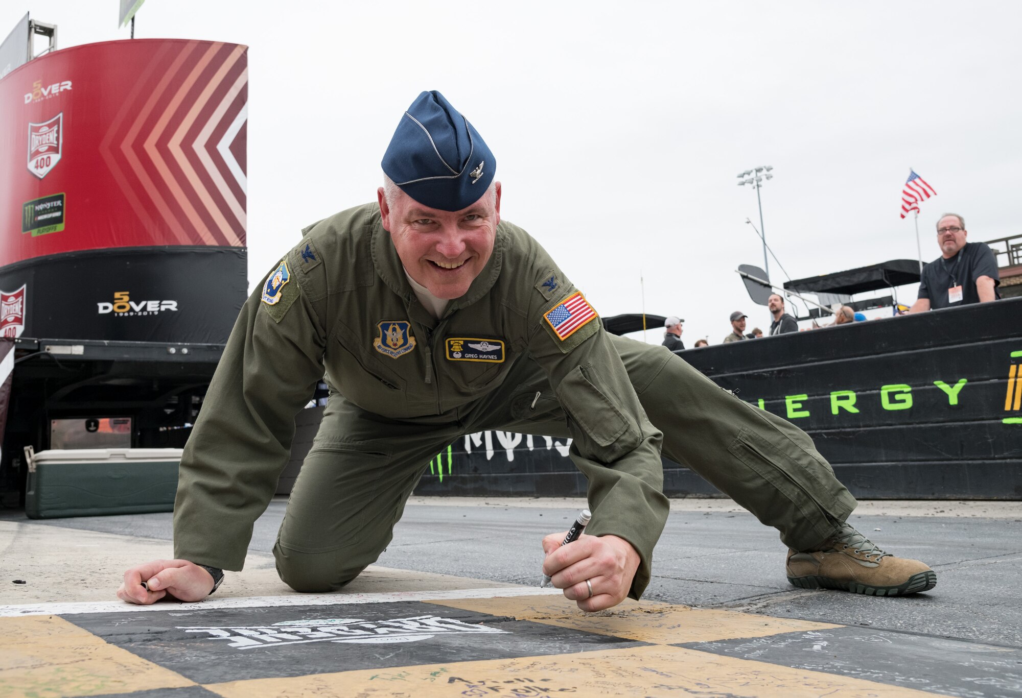 Col. Gregory Haynes, 512th Airlift Wing commander, writes on the racetrack start/finish line Oct. 6, 2019, at Dover International Speedway, Dover, Del. Haynes took the opportunity to write a message on the checkered line prior to the start of the “Drydene 400” Monster Energy NASCAR Cup Series playoff race. (U.S. Air Force photo by Roland Balik)