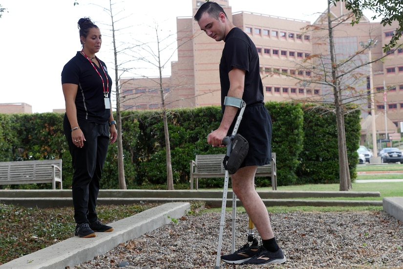 Physical therapist observes as man with prosthetic leg works on learning to walk.