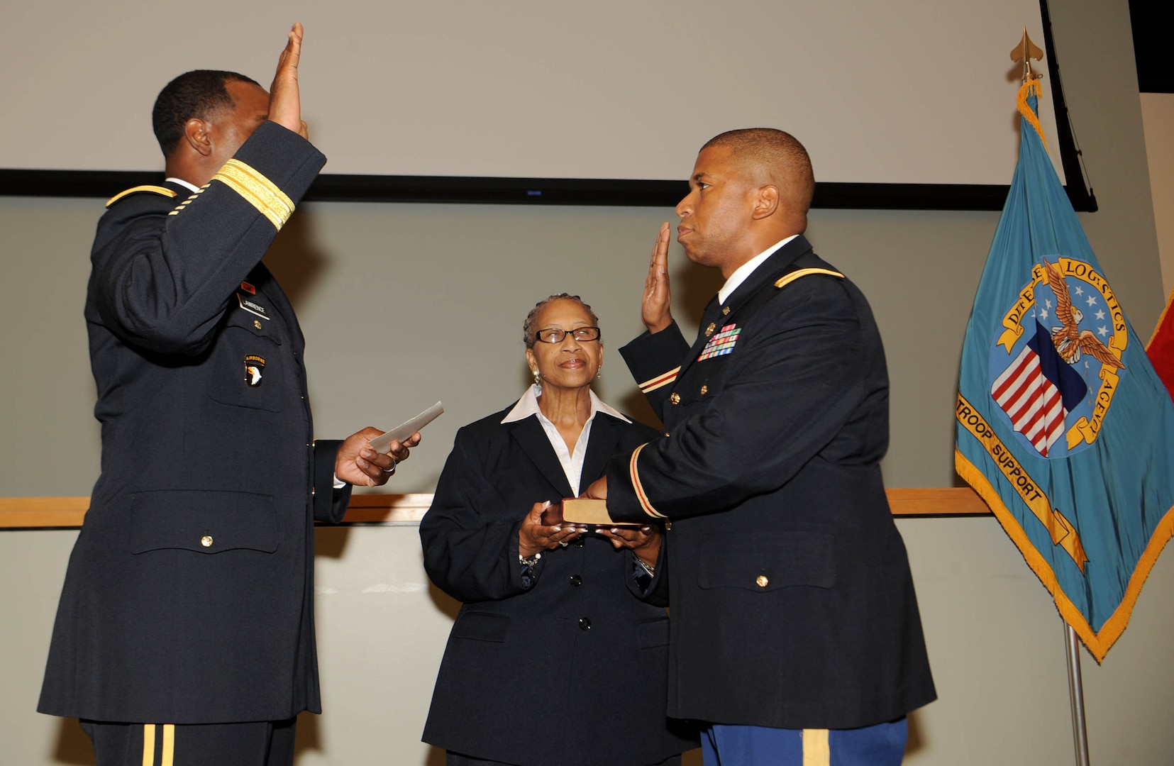 Army Col. Eric McCoy, right, reaffirms the oath of the commissioned officer with Brig. Gen. Gavin Lawrence, DLA Troop Support commander, left, as his mother, Arlene Fair, center, holds the Bible during a promotion ceremony in Philadelphia, Oct. 3, 2019. McCoy, a Baltimore native, is the Troop Support Subsistence supply chain director.
