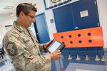 Master Sgt. Alan Romero, 167th Airlift Wing airfield manager, looks at a schematic showing where visual landing zone marker panels would be placed on an airfield for assault landing practice. The orange VLZMP in the photo was designed and fabricated at the 167th AW. Romero, and the airfield management team, are working with officials at the John Murtha Johnstown-Cambria Airport in Johnstown, Pa., to use a runway there for C-17 Globemaster III aircraft assault landing practice. The VLZMP are just one step in a lengthy approval process. (U.S. Air National Guard photo by Senior Master Sgt. Emily Beightol-Deyerle)