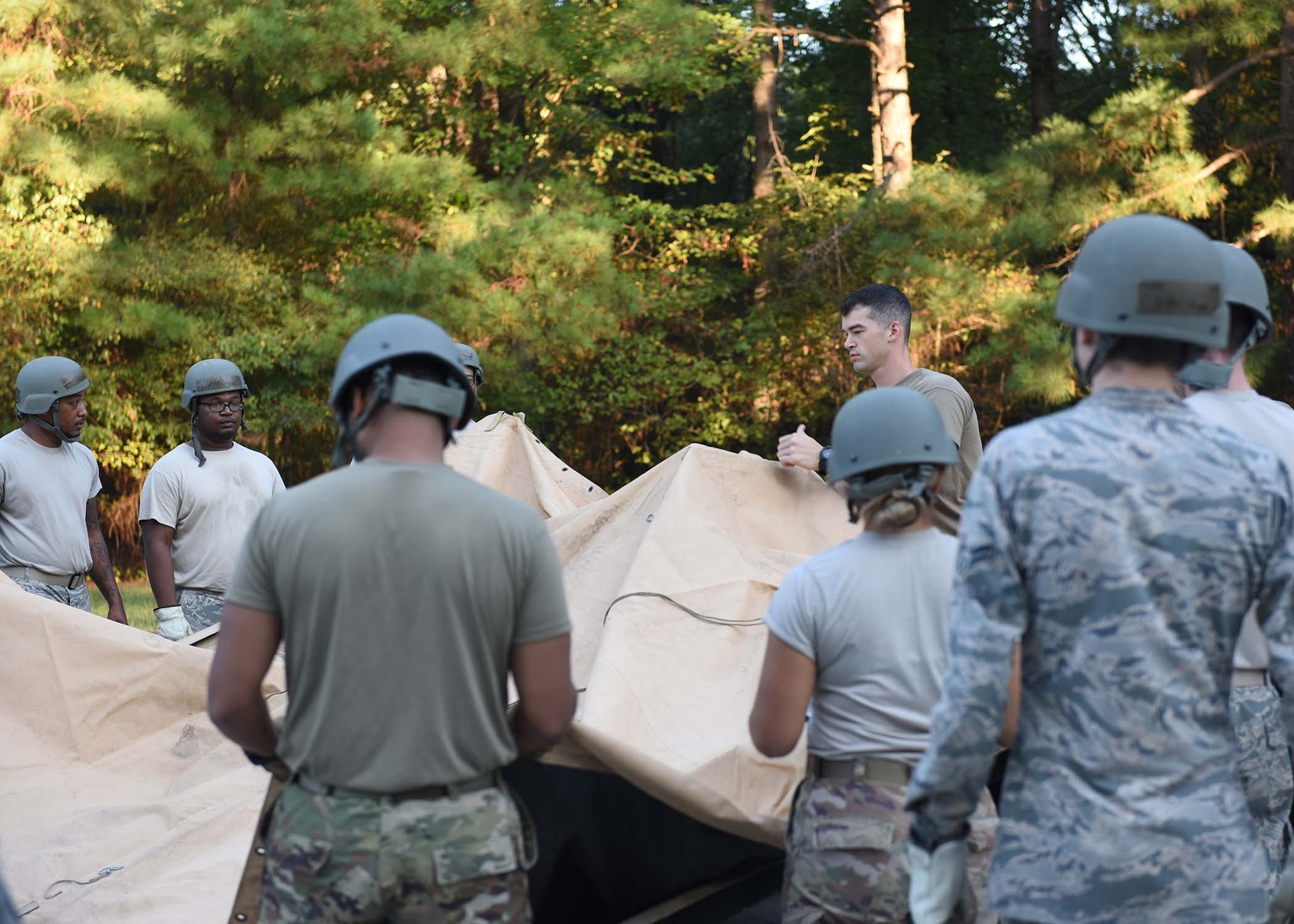 Multiple Airmen spread a plastic cover over a tent.
