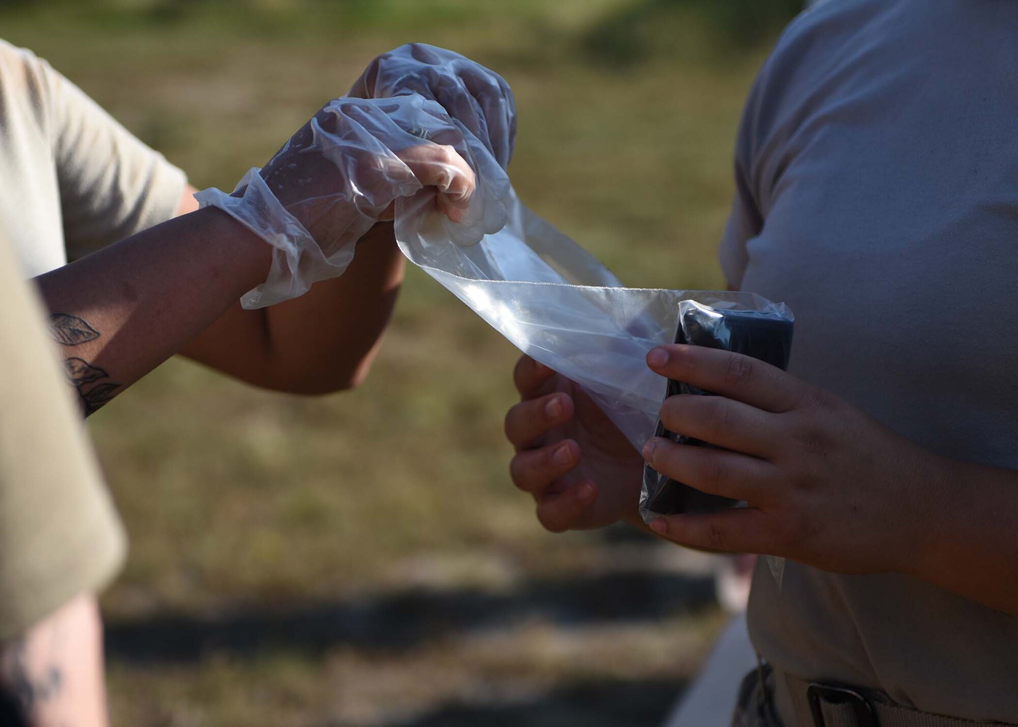 Two Airmen place a black wallet inside a plastic bag.