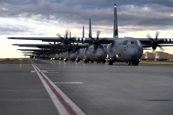 C-130s taxi down a runway in a formation.
