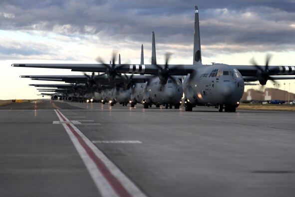 C-130s taxi down a runway in a formation.