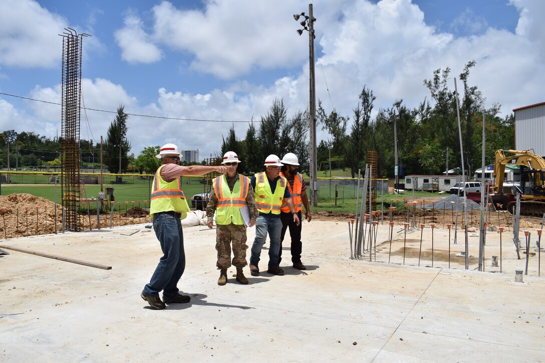 Four men wearing personal protective gear walk around a military construction site