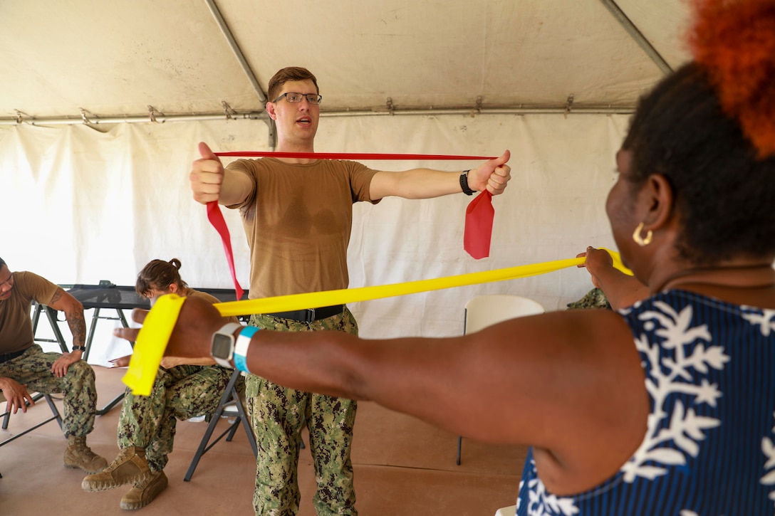U.S. Navy Hospital Corpsman teaches a woman mobility exercises.