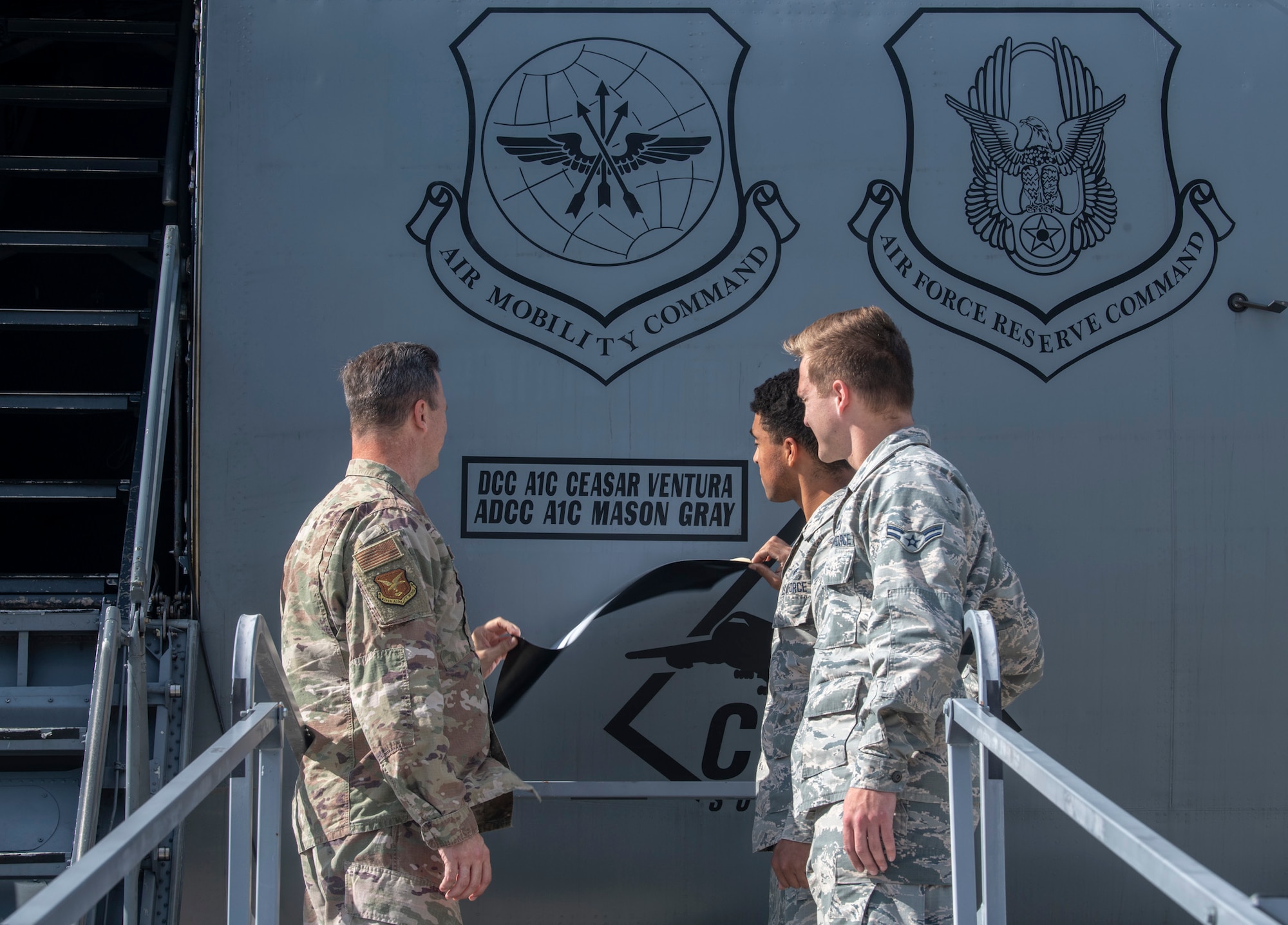 Col. Joel Safranek, 436th Airlift Wing commander, Airman 1st Class Ceasar Ventura, 436th Aircraft Maintenance Squadron dedicated crew chief, and Airman 1st Class Mason Gray, 436th AMXS assistant dedicated crew chief, pull off tape during a DCC unveiling ceremony Oct. 4, 2019, at Dover Air Force Base, Del. A change in policy marked the first time in approximately 20 years that the names of dedicated crew chiefs were unveiled on an Air Mobility Command C-5M Super Galaxy and C-17 Globemaster III.  (U.S. Air Force photo by Senior Airman Christopher Quail)