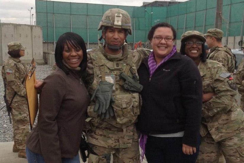 Two women pose for a photo with a man dressed in a military uniform.