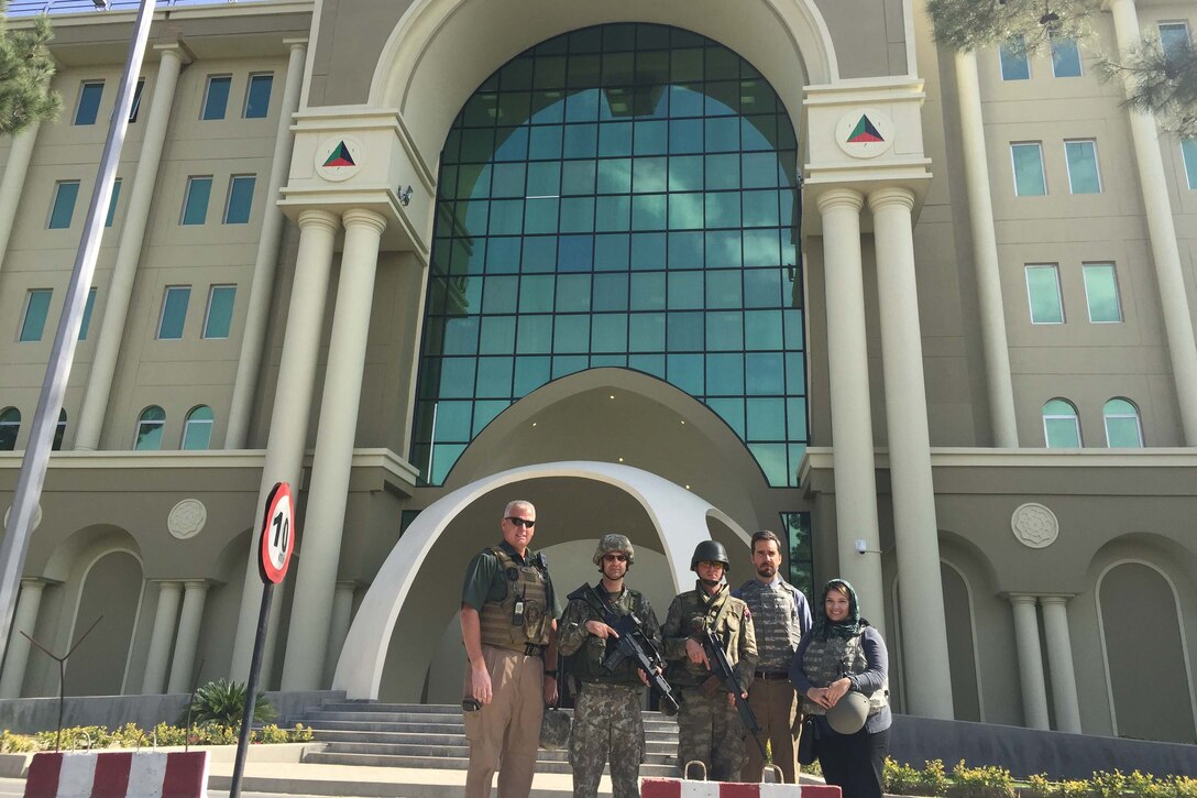 Five people pose for a photo in front of a large building.