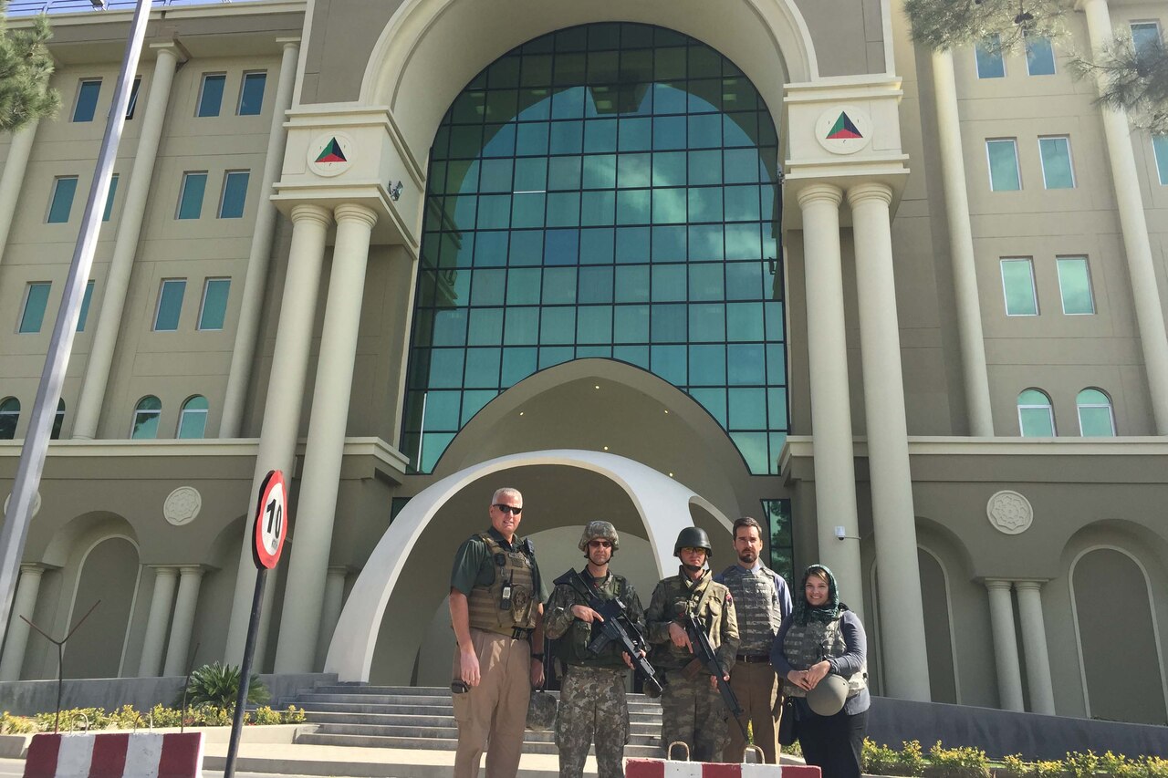 Five people pose for a photo in front of a large building.