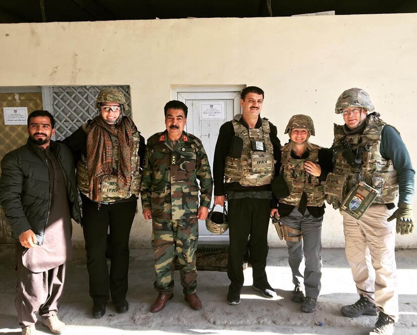 Six people pose for a photo in front of a small building with a white door.
