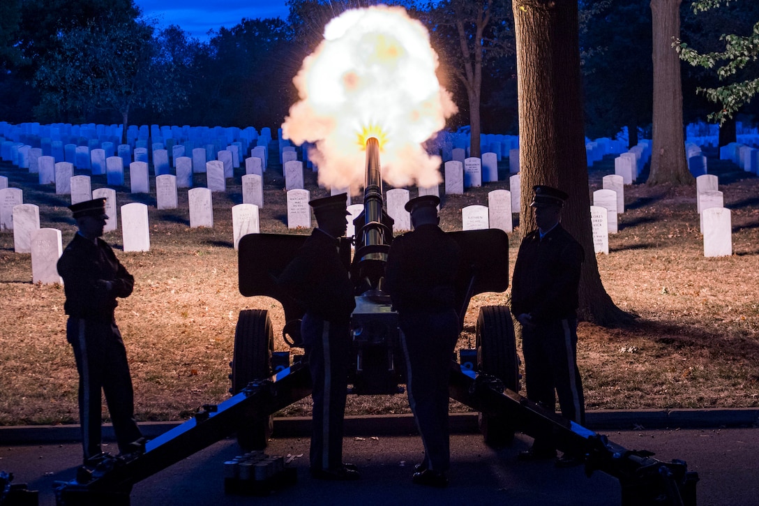 Soldiers fire a cannon at a cemetery at night.
